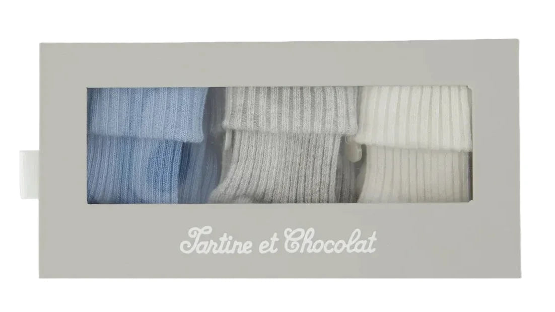 Presented in a rectangular box with a window, the Tartine et Chocolat Cotton Sock Set features three pairs of ribbed baby socks in blue, gray, and white. Designed for sensitive baby skin, these toddler socks are packaged with “Tartine et Chocolat” printed on the box.