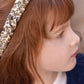 A young child with light skin and long brown hair is seen in profile, wearing the Tartine et Chocolat Liberty Print Braid Headband and a navy blue sweater, gazing off to the right.