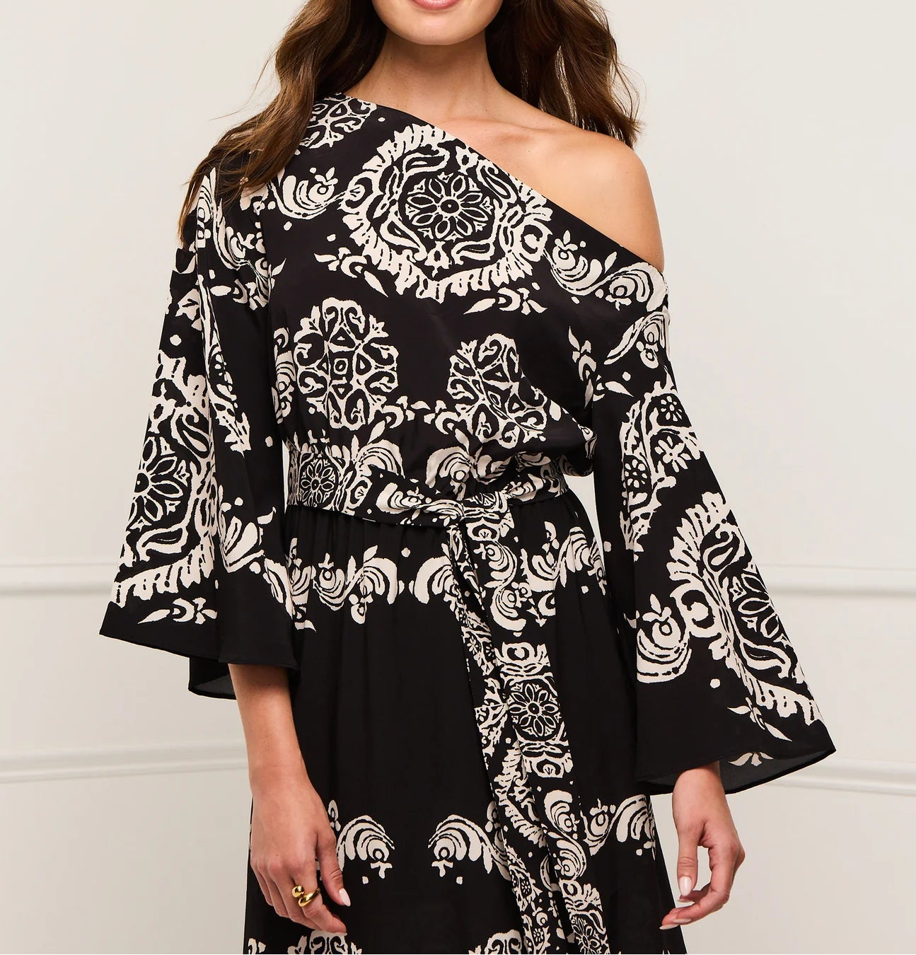 A woman models the Figue Christy Dress, a black and white patterned one-shoulder viscose crepe design with wide sleeves and an elastic waistband, against a plain background.