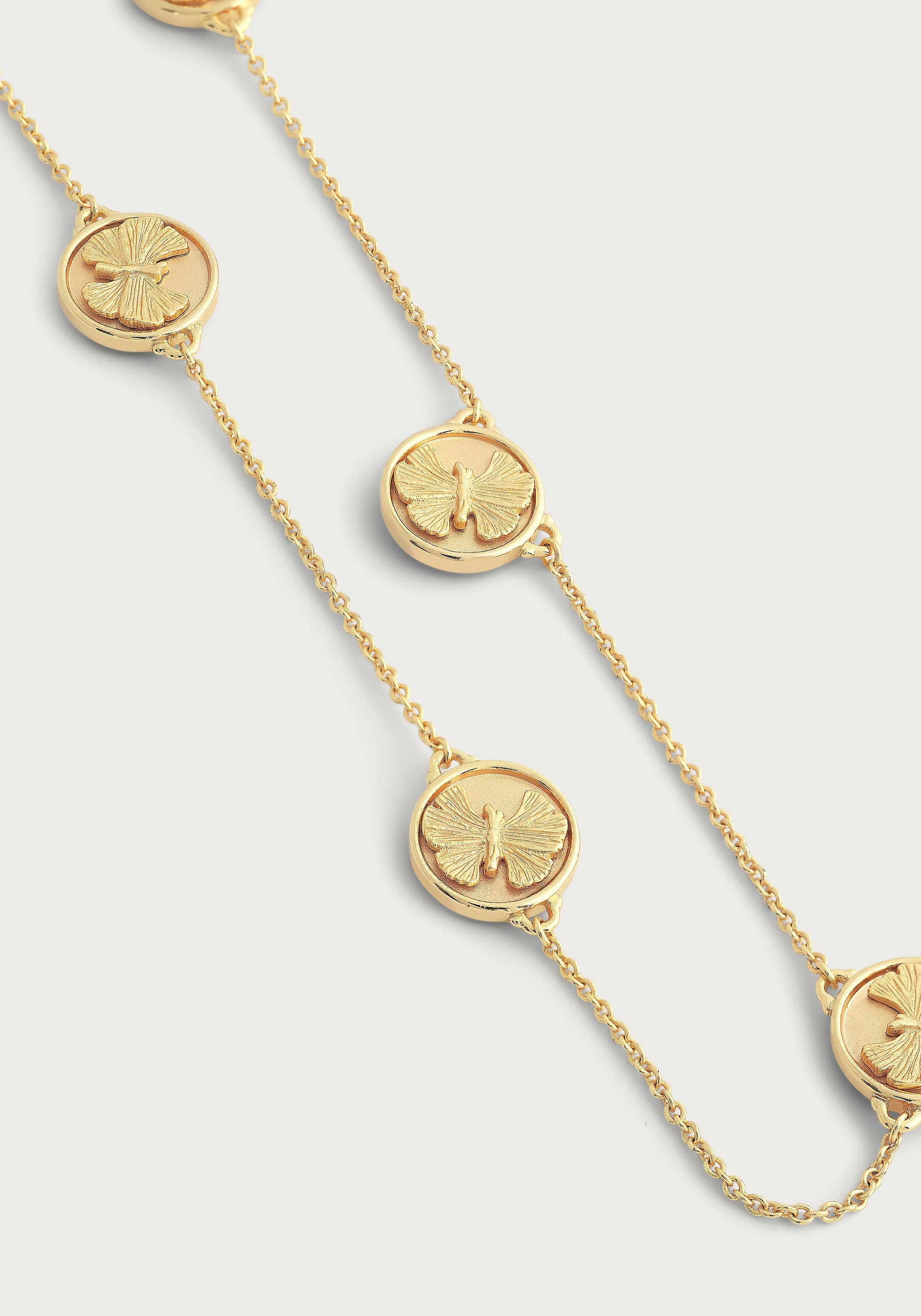 The Anabel Aram Butterfly Coin Station Necklace features round medallion pendants with raised butterfly designs in an 18k gold dipped finish, elegantly displayed on a plain background.