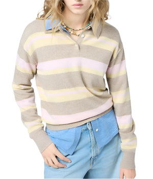 A person wears the Guest in Residence Collegiate Stripe Polo in beige with pastel pink and yellow stripes over a blue collared shirt and light blue jeans, standing with one hand in their pocket.