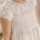 Child wearing the Antoinette Girls' Colombe White Silk Dress, featuring puff sleeves, a smocked bodice, and a frilled collar—perfect for special occasions.