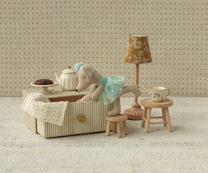 The Maileg Dance Mouse in Daybed, Little Sister, wears a blue dress and stands on a stool by a makeshift table with tiny tea set, cake, lamp, and daybed close by.