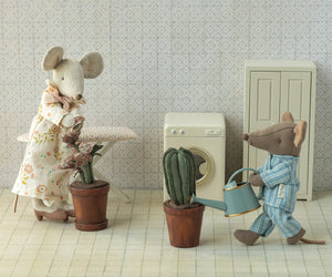 Maileg’s Watering Can, Mouse—Light Blue—features two mice in pajamas and a dress, tending plants in a tiny laundry room with washing machine and cabinet, making a charming accessory for any scene.