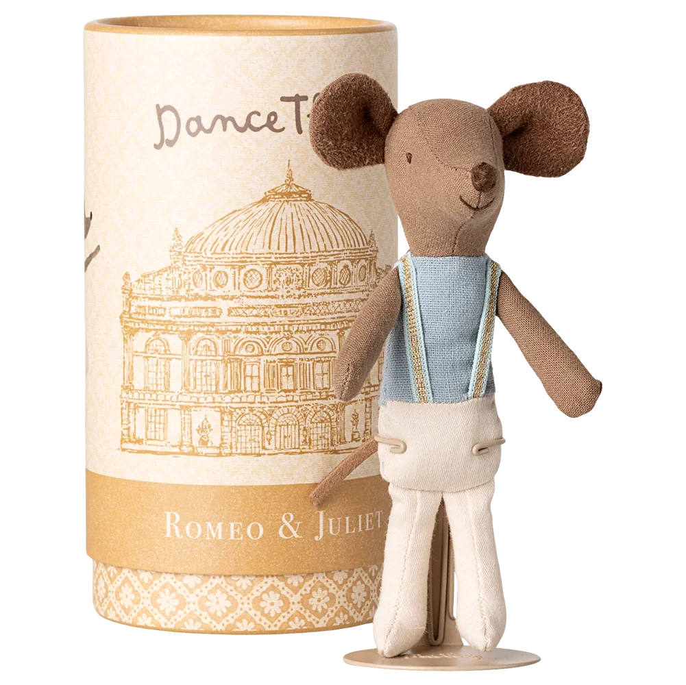 A Maileg Ballet Dancer Mouse, Big Brother, in a blue top and white pants stands before a cylindrical "Romeo & Juliet" box featuring a building illustration.