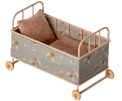 The Maileg Cot Bed, Micro – Powder is a small beige metal bed with floral fabric sides, wooden wheels, a soft mattress, and two checkered pillows—ideal for your micro sized friends.