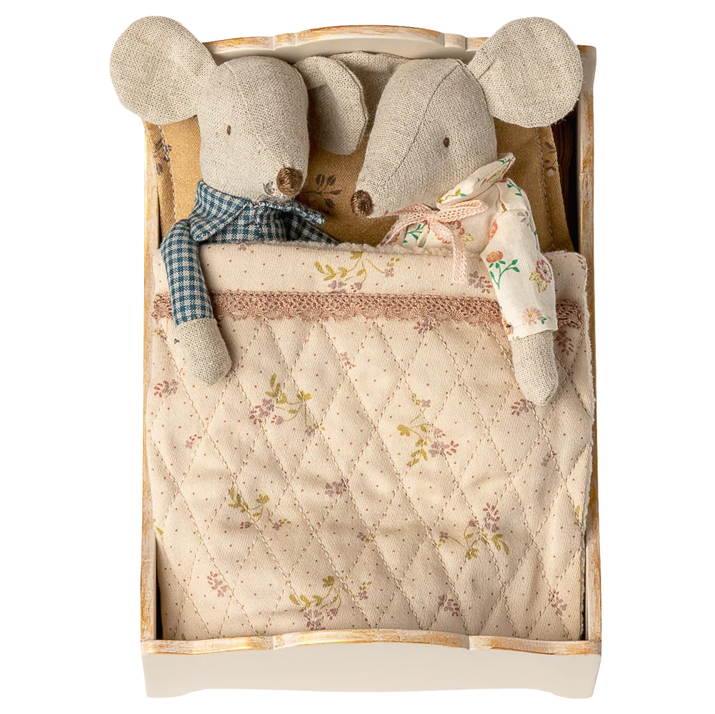 Two Maileg fabric mice dressed in pajamas rest side by side in the Bed, Mouse - Off White, tucked under a patterned quilt for a cozy scene.