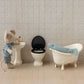 A Maileg Off White Water Closet - Mouse stands by a sink next to a compact toilet, with a plush fish resting in a small bathtub—all arranged in a charming miniature bathroom scene.