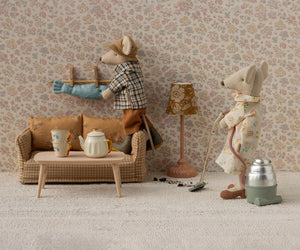 Two toy mice from Maileg tidy their miniature living room; one vacuums while the other hangs laundry. The cozy scene features the Maileg Couch, Mouse - Mable, a table with tea set, and a lamp.