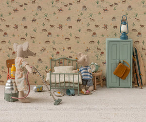 Two toy mice in a miniature room: one vacuums while the other stands by a Maileg Vintage Single Bed, Mouse - Mint. The scene features Maileg bedding, a green cabinet, scattered items, and wallpaper with western-themed illustrations.