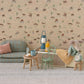 A charming miniature living room featuring Maileg’s Vintage Chair, Mouse - Mint, with tiny furniture, a toy mouse, lamp, clock, cups, bottle, and bread slice—all set against a patterned wall and carpeted floor.