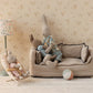 Three micro-sized Maileg rabbits relax in a dollhouse living room, featuring a sofa, lamp, soft toy ball, and the Maileg Babysitter, Micro - Off White.