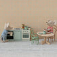 In a miniature Maileg scene, two toy mice enjoy their time with the Kitchen Counter - Mouse: one mouse stands at the detailed kitchen counter cooking up tasty meals, while the other relaxes at a round table set with mugs and a plate.