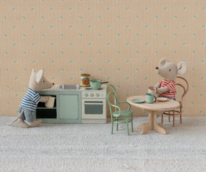 In a miniature Maileg scene, two toy mice enjoy their time with the Kitchen Counter - Mouse: one mouse stands at the detailed kitchen counter cooking up tasty meals, while the other relaxes at a round table set with mugs and a plate.