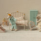 Three Maileg My-size mice in a miniature bedroom: one in bed, the Babysitter (My - Rose) holding a baby mouse, and another mouse in a bunny chair, with a clock, cabinet, and folded bedding in the background.