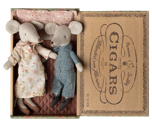 Grandma and Grandpa Mice in Cigarbox by Maileg rest together in their cozy bed, dressed in a floral dress and checked overalls, nestled side by side with a soft pillow and blanket.