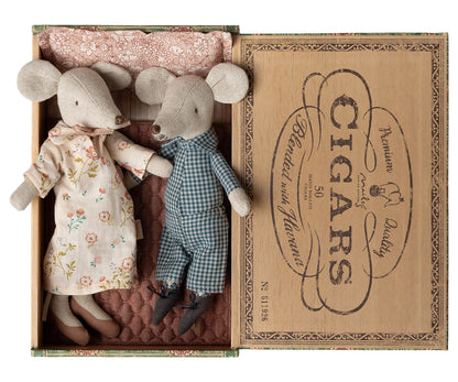Grandma and Grandpa Mice in Cigarbox by Maileg rest together in their cozy bed, dressed in a floral dress and checked overalls, nestled side by side with a soft pillow and blanket.