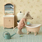 A Maileg Rose Bathtub – Mouse features a plush mouse in pajamas beside a vintage-inspired bathtub in the charming Mouse Hole Farmhouse bathroom, complete with a sink, mirror, toilet, watering can, and bottle on a patterned floor—perfect for the whole mouse family.