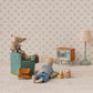 Two toy mice enjoy a cozy evening at Mouse Hole Farmhouse; one relaxes in a chair with a mug while the other lounges on the floor with snacks. Surrounded by charming miniature mouse accessories from Maileg, including their Television - Mouse, as well as a lamp and bag, they unwind together against a floral patterned backdrop.