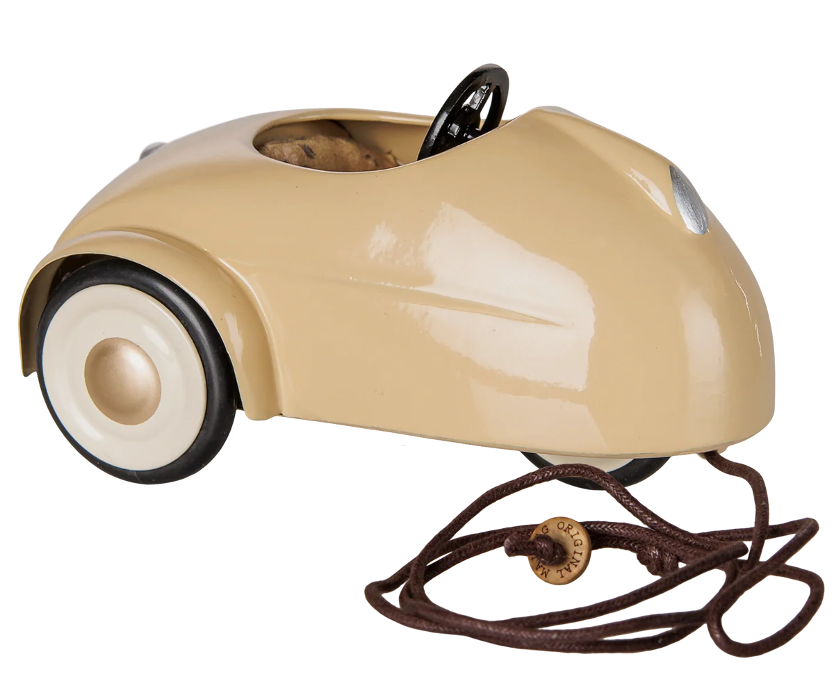 The Maileg Car, Mouse - Wheat is a beige metal car featuring a black steering wheel, white wheels, and a pull string attached to the front—perfect as a pull-along toy or for imaginative play with toy mice, shown against a plain background.