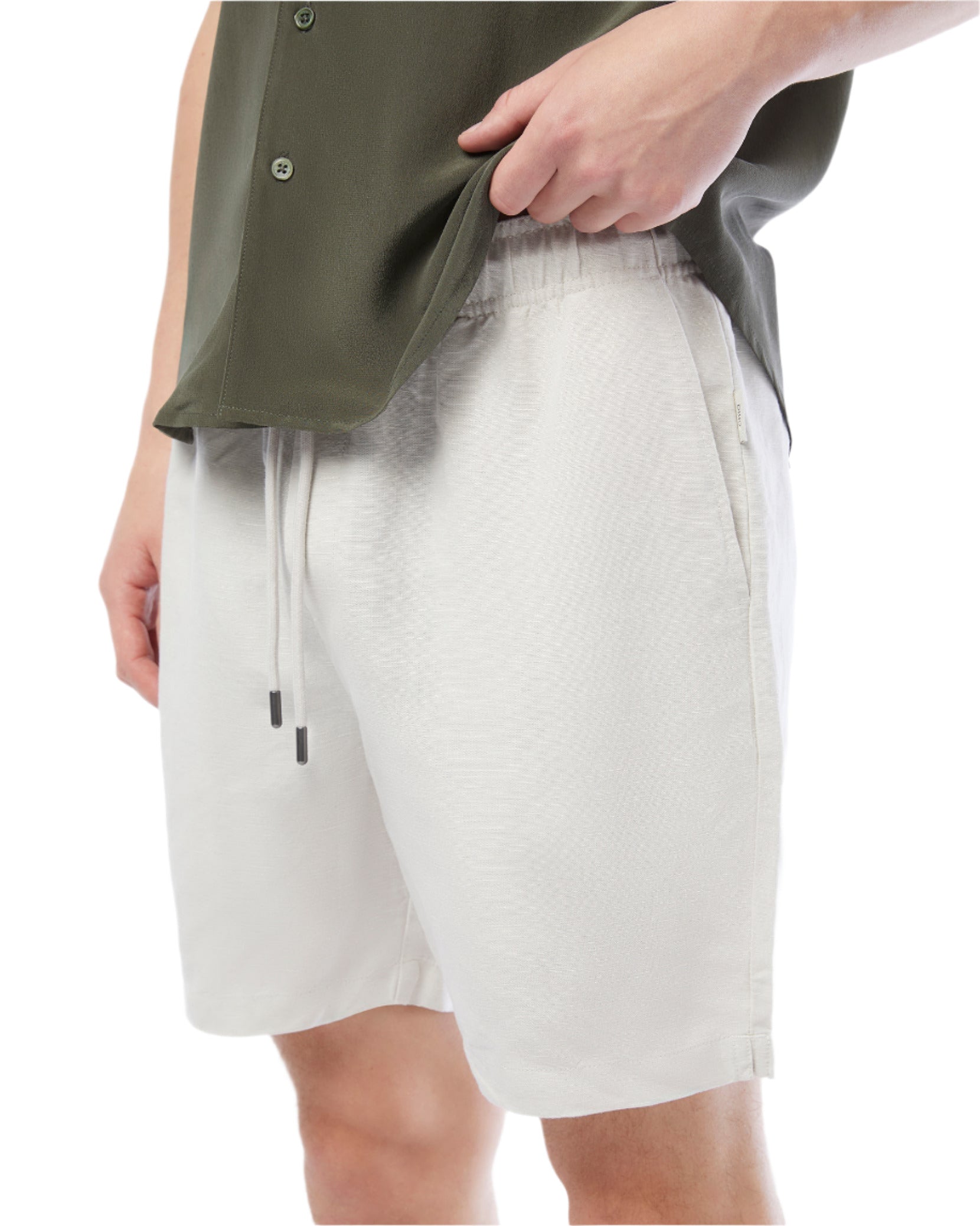 A person in a green shirt and Onia's Air Linen Pull-On Short in white, made from a linen-tencel blend, casually holds the shirt hem with their left hand.