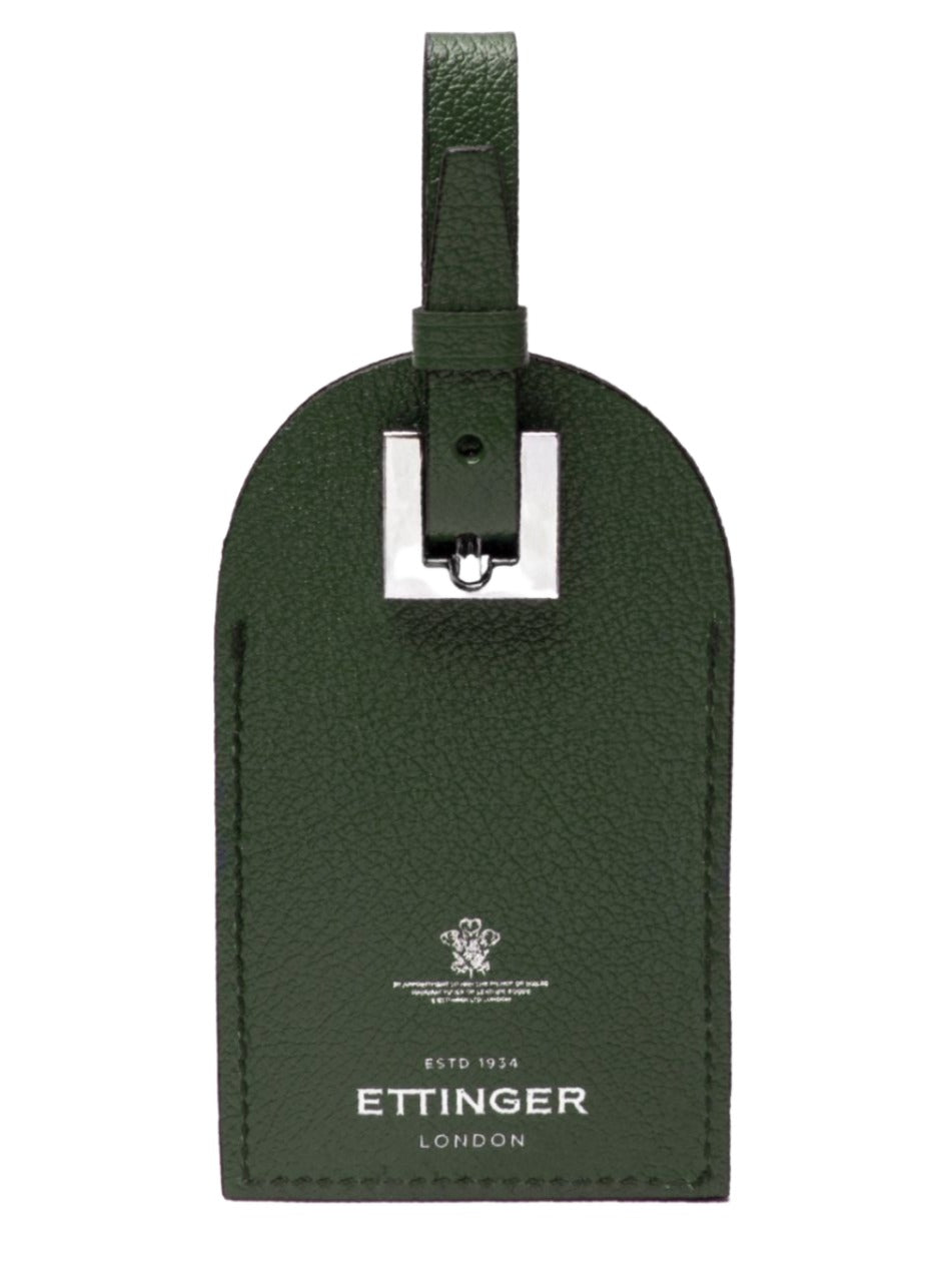 The Capra Luggage Tag with Security Flap by Ettinger is an elegant green tag crafted from premium goat leather, featuring a silver buckle and embossed with "Ettinger London" alongside a crest.