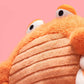 Close-up of the Jellycat Pinchsnap Crab, an orange plush toy with big eyes and a ribbed belly, shown against a solid pink background.