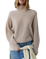 A woman wears the Guest in Residence Cropped Ribbed Turtleneck with blue jeans and a light sweater tied around her waist.