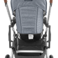 View of the rear side of a gray UPPAbaby Cruz V2 Stroller, showcasing its brown handlebars, black wheels, and a storage basket underneath. The light frame is designed to support a reversible Toddler Seat and features a UPF 50+ canopy for sun protection.