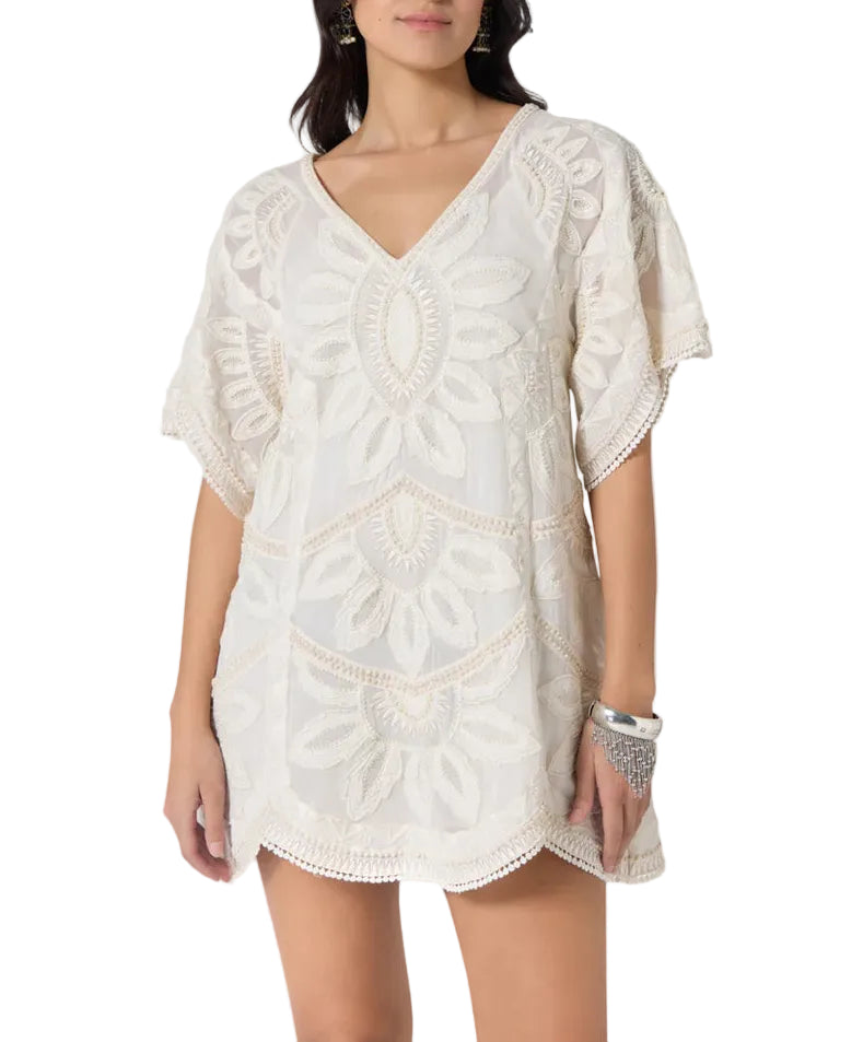 A woman models the Scarlett Poppies Ulay Dress, a short, loose-fitting white dress with embroidery, short sleeves, V-neckline, and artisanal details, styled with a bracelet.