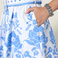 Wearing the Scarlett Poppies Vixeen Dress with blue floral and bird prints, French knot details, a matching belt, and a silver bracelet, their hand rests casually in the dress pocket.