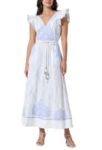 A woman wears the Scarlett Poppies Vittorio Dress—a white sleeveless maxi with a feminine silhouette, ruffle shoulders, blue statement embroidery, tie waist—and pairs it with white strappy sandals.