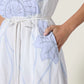 Someone wearing the Scarlett Poppies Vittorio Dress, featuring light blue statement embroidery, a white cord belt, and their right hand placed in the dress pocket.
