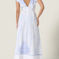 A woman models the Vittorio Dress by Scarlett Poppies, showcasing statement embroidery, ruffled cap sleeves, a deep V-back, and a feminine silhouette. She pairs it with white heeled sandals against a plain backdrop.
