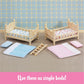 Two small wooden Calico Critters Stack and Play Beds with patterned bedding, a ladder, blue and pink bedding sets, plus pillows are arranged on a carpeted floor against a plaid wallpaper backdrop—perfect as dollhouse furniture.