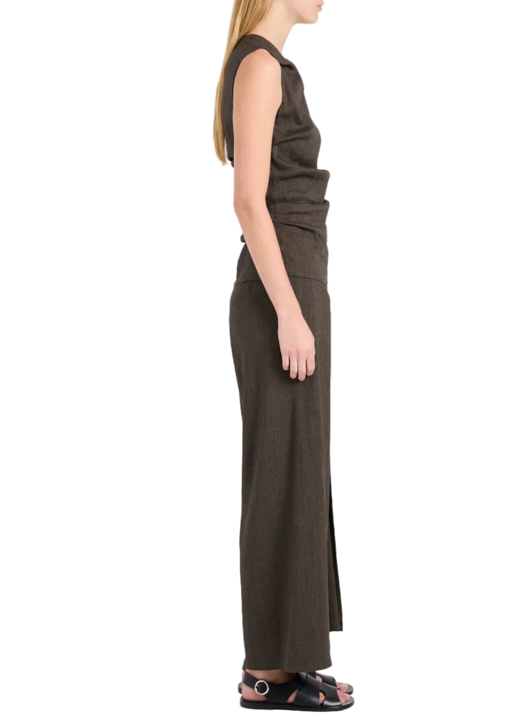 A woman stands in profile wearing a sleeveless brown top, black sandals with silver buckles, and the Calla Slub Linen Pant by Proenza Schouler White Label—wide-leg with a front leg wrap.