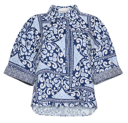 The Cara Cara Calvia Top is a blue and white button-down blouse with geometric and floral prints, a collared neckline, and classic short sleeves—an easy update to your camp shirt collection.