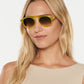 A woman with long blonde hair wears Krewe Cameron Sunglasses—yellow acetate frames with round lenses—and a beige sleeveless top, posing against a plain white background.