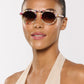A person models Krewe's Cameron Sunglasses with colorful round lenses and a signature brow bar, paired with a beige halter top, against a plain white background.