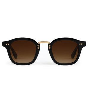 The Krewe Campbell Sunglasses have black square acetate frames, brown gradient lenses, and a gold bridge with precious metal accents, shown against a white background.