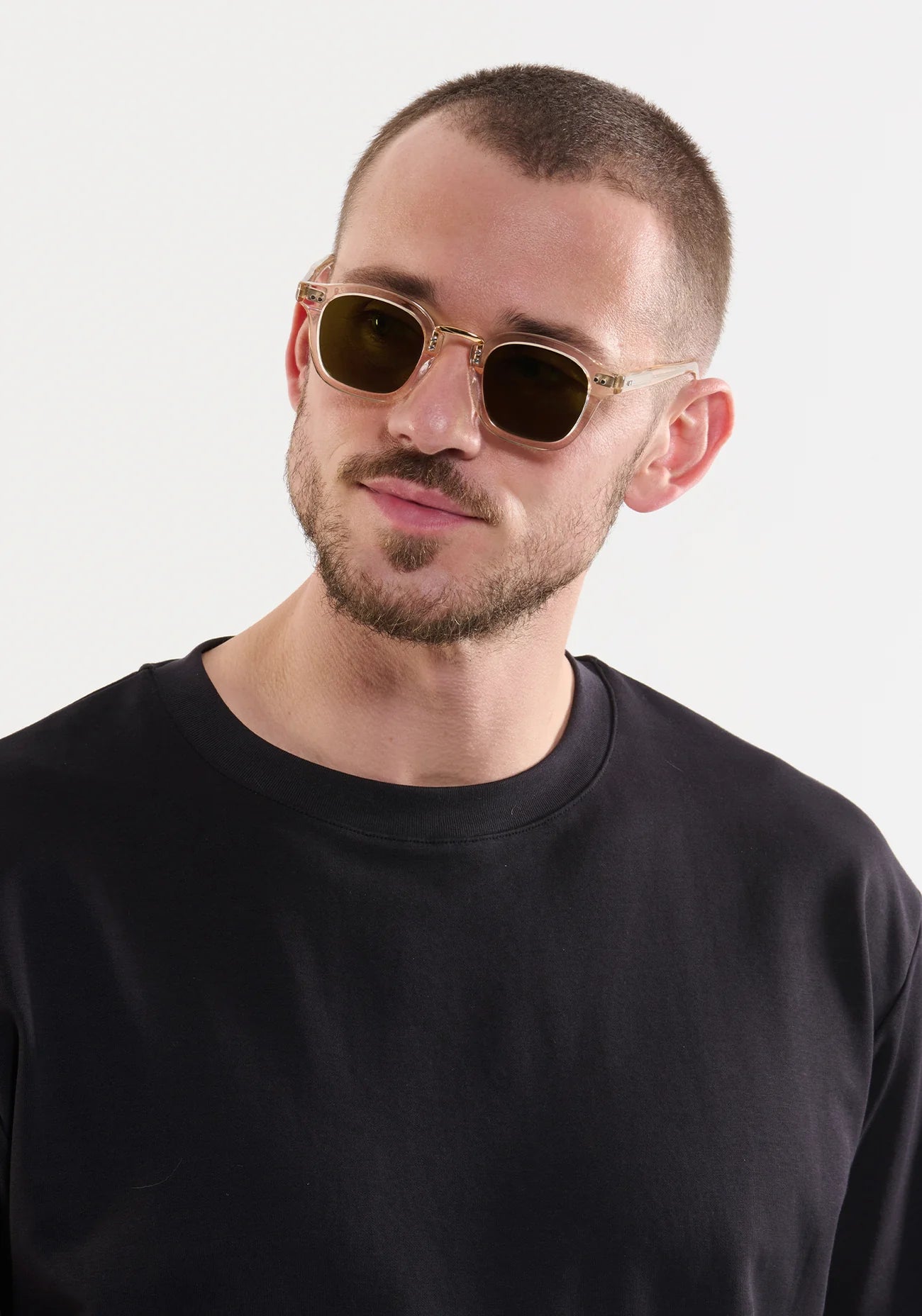 A man with a short beard and buzz cut wears Krewe’s Campbell Polarized Sunglasses and a black crew-neck shirt against a plain light background.
