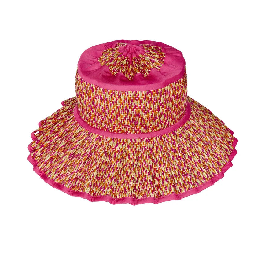 The Island Capri Hat by Lorna Murray features a wide brim and a pink, yellow, and white woven pattern with a solid pink top and brim edge. Offering UPF 50+ protection, this travel-ready hat is displayed on a white background.