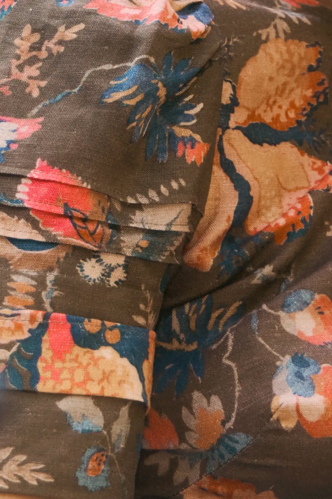 Close-up of folded fabric with a floral pattern in blue, peach, pink, and beige on brown—ideal for crafting the universally flattering Casey Dress by Hunter Bell NYC.