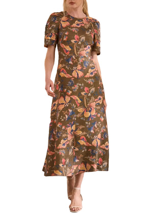 A woman wears the Hunter Bell NYC Casey Dress—an ankle-length, versatile brown dress with a vibrant floral print and short puffed sleeves—paired with open-toe heels.