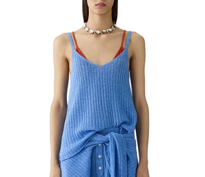 A woman wears the Breezy Rib Tank by Guest in Residence—a blue v-neck rib knit top—layered over an orange undergarment, paired with a matching blue skirt and chunky beaded necklace, ideal for summer styling.