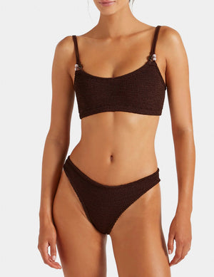 Model is wearing the Hunza G Cassie Bikini in dark brown, featuring a textured finish with a scoop neck top and high-cut bottoms, standing against a plain background.