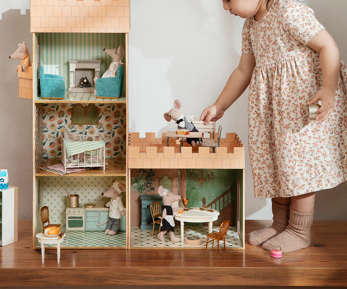 A child in a floral dress embarks on a palace adventure, playing with the Maileg Castle Hall by Maileg, featuring miniature mice figures in various rooms. Recommended age 3+.