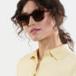 Woman with wavy brown hair wears Krewe’s Celeste Polarized Sunglasses, featuring a classic tortoiseshell frame, paired with a light yellow collared shirt against a plain white background.