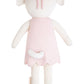 Charlotte the Dog - Regular 20" by Cuddle + Kind is a knitted plush animal doll with cream-colored limbs and head, a short tail, and wears a light pink dress with a matching wildflowers headband, shown from the back.