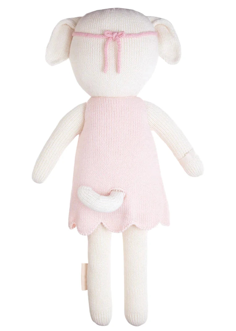 Charlotte the Dog - Regular 20" by Cuddle + Kind is a knitted plush animal doll with cream-colored limbs and head, a short tail, and wears a light pink dress with a matching wildflowers headband, shown from the back.